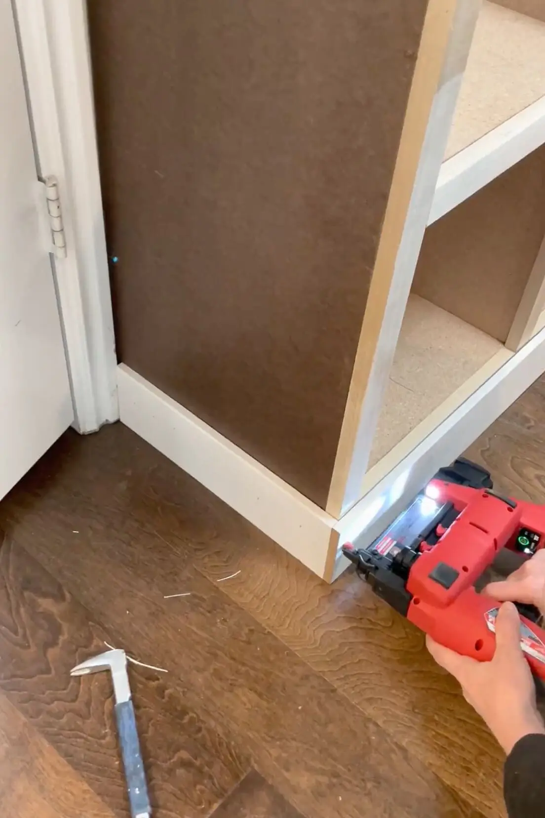 Using a nail gun to attach baseboard trim to a built-in storage cabinet for a seamless, finished look.